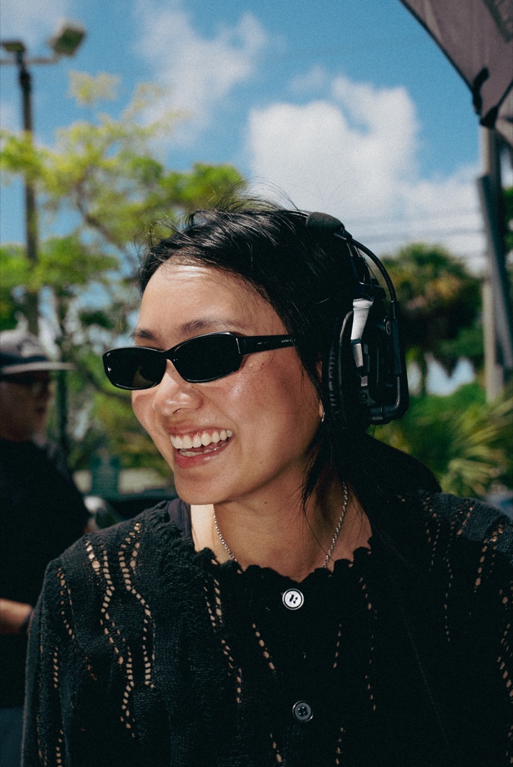 A crew member on headset between setups, smiling on a sunlit location